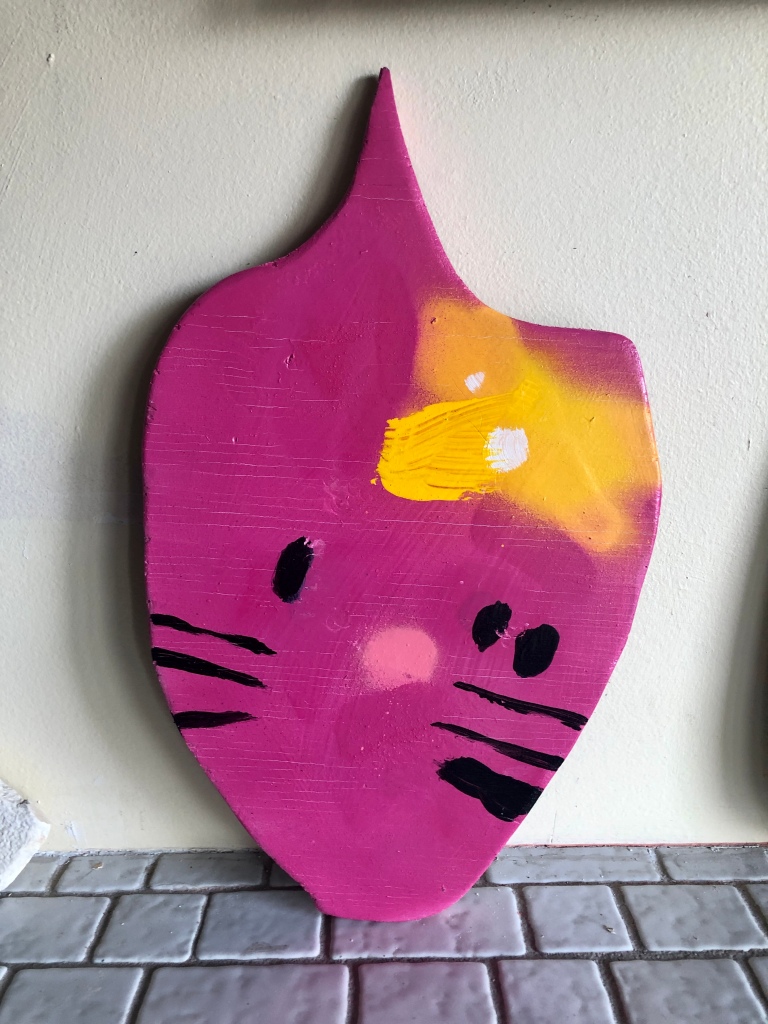 This 2010 Anthony Lister artwork on plywood is a pink kitty with black whiskers and eyes, along with a yellow bow.